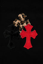 Black fabric pants with leopard and red cross appliques close-up.