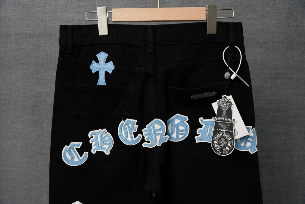 Chrome pants on hanger, black with blue cross patches and a keychain detail tag