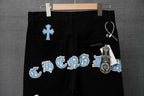 Chrome pants on hanger, black with blue cross patches and a keychain detail tag