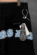 Black pants with blue and white cross patches and a small hanging charm