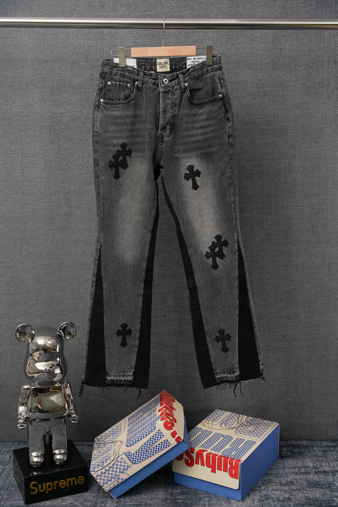 Black denim pants with four-petal cross graphics on both legs, front view.