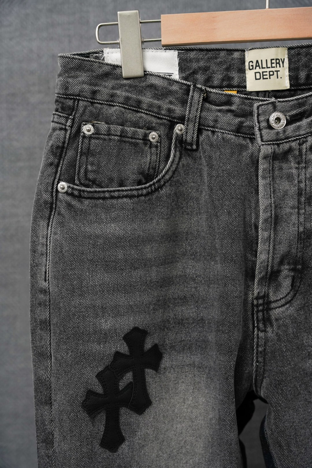 Dark denim pants with curved front pockets and large cross emblem near hem