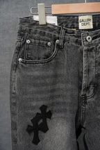 Black denim pants with curved front pockets and four-petal cross graphic on front leg.