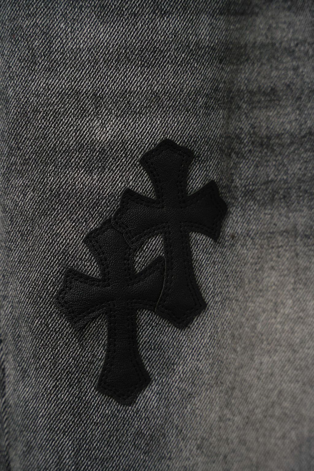 Black denim pants fabric detail with four-petal cross graphic, close-up.