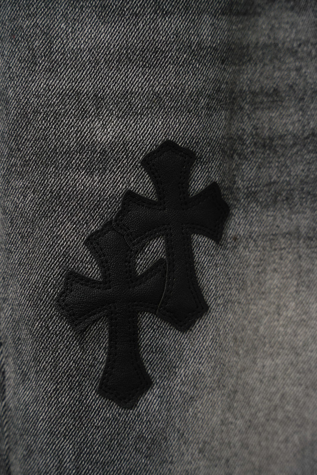 Black denim pants fabric detail with four-petal cross graphic, close-up.