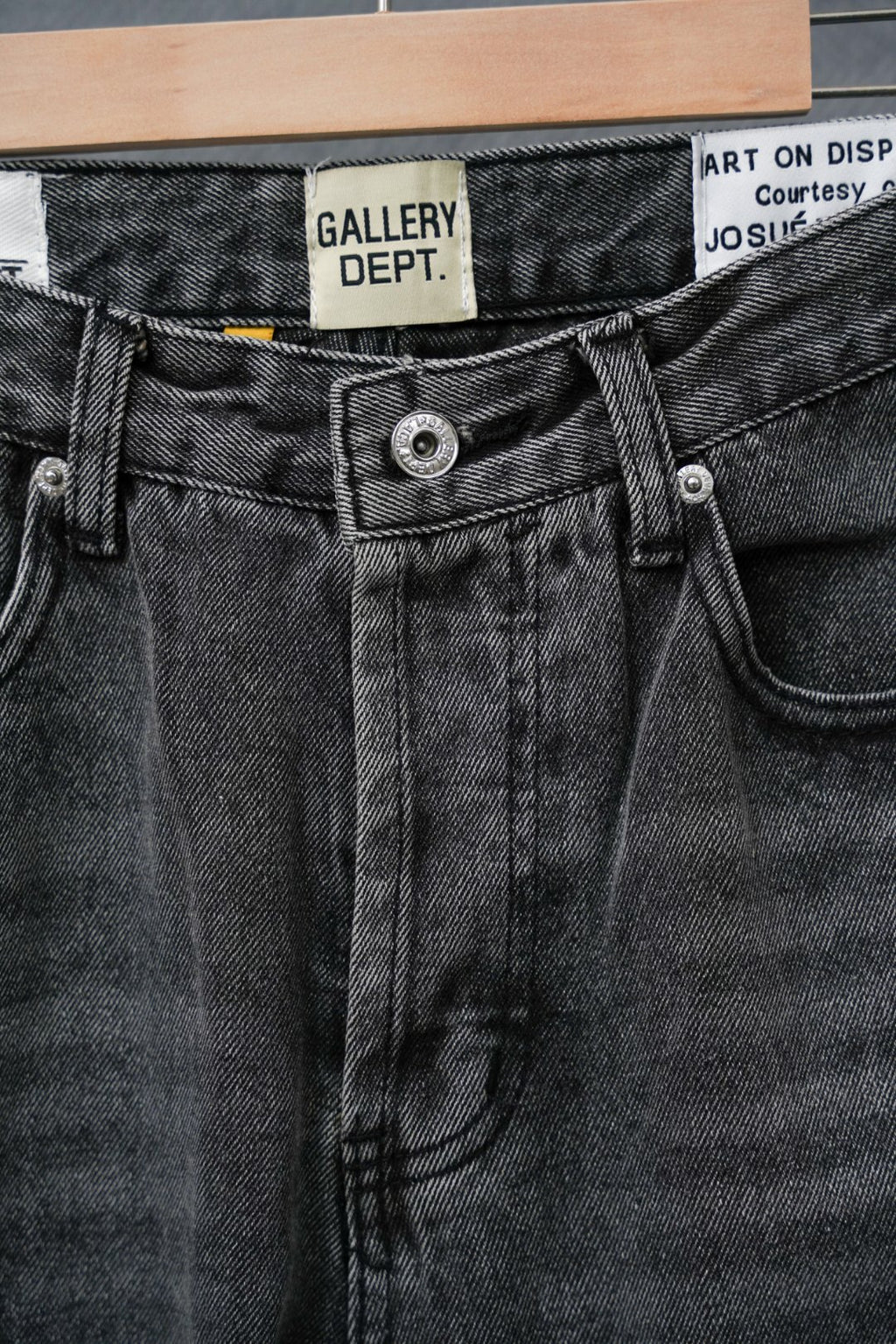 Black denim pants with contrast belt loop and button closure, close-up of waistband.