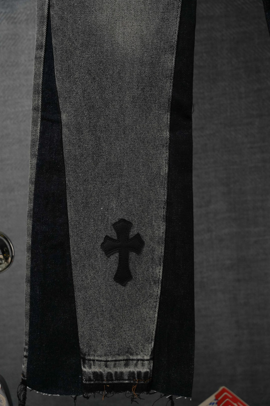Dark denim pants leg with cross emblem near the cuff