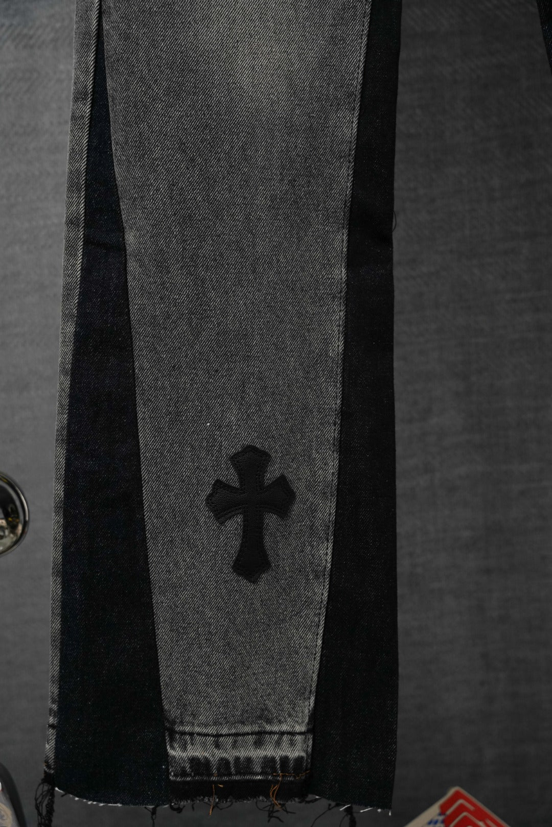 Black denim pants detail with four-petal cross graphic near hem.