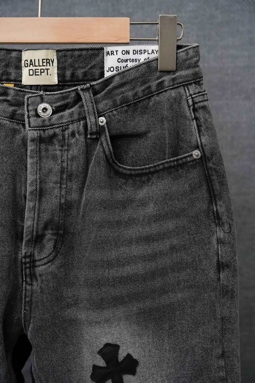 Black denim pants with front button fly and four-petal cross graphic on thigh.