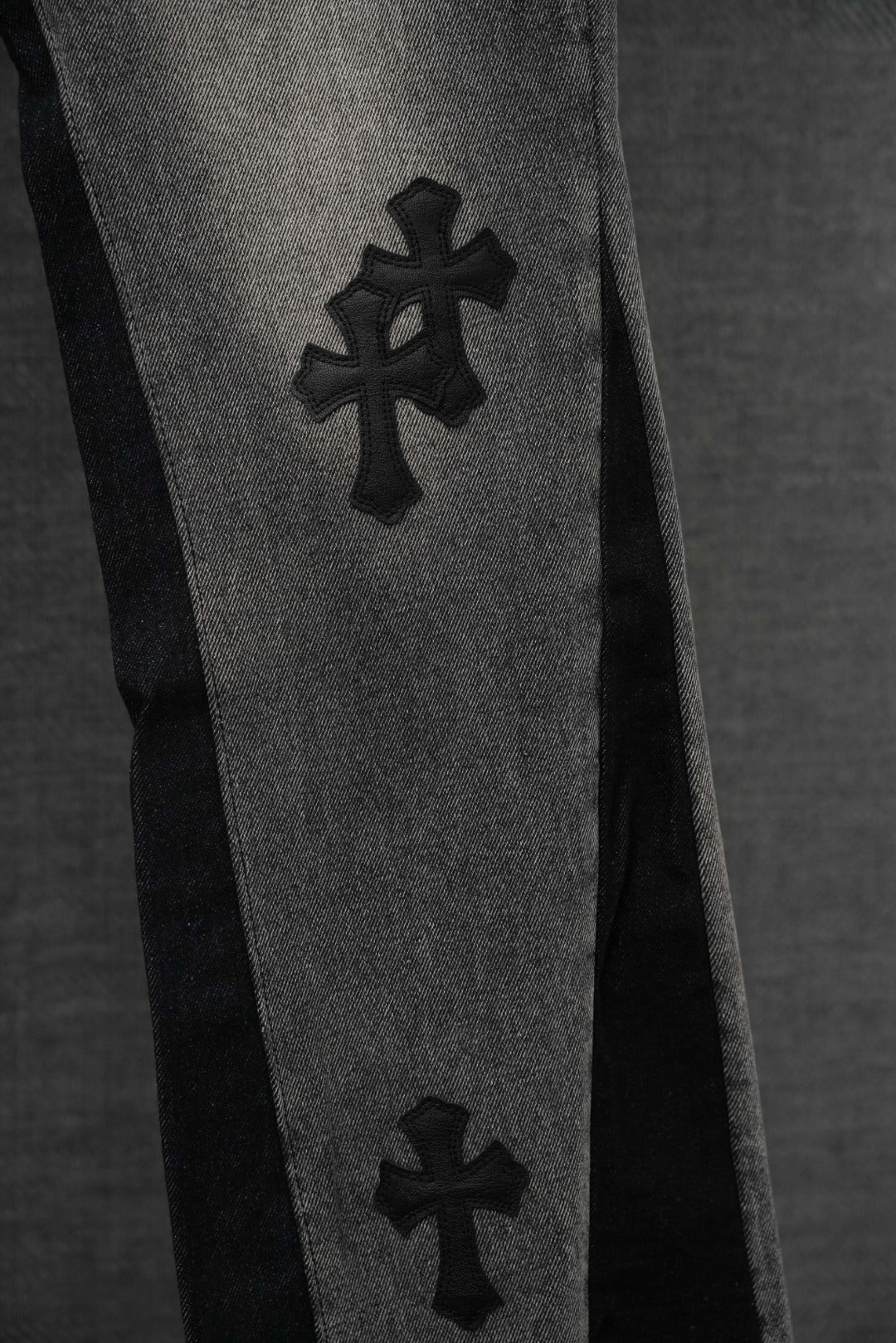 Close-up of dark denim pants leg with cross emblem print
