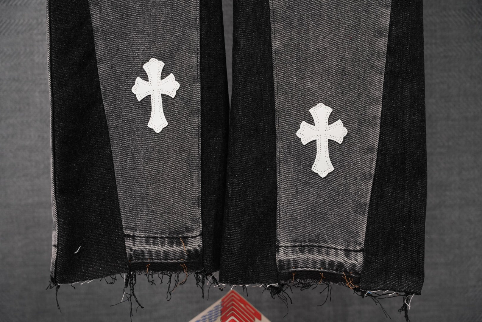 Dark gray denim pants with white cross patches, distressed frayed hem