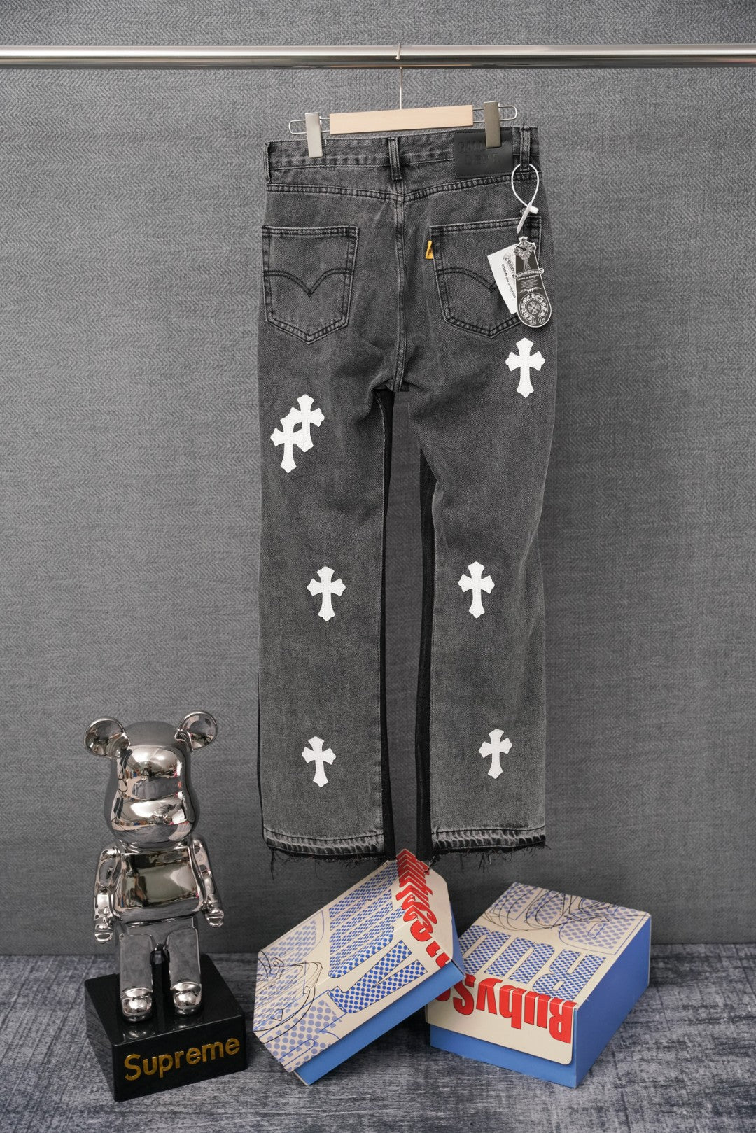 Dark gray denim pants with repeated white cross patches, front view