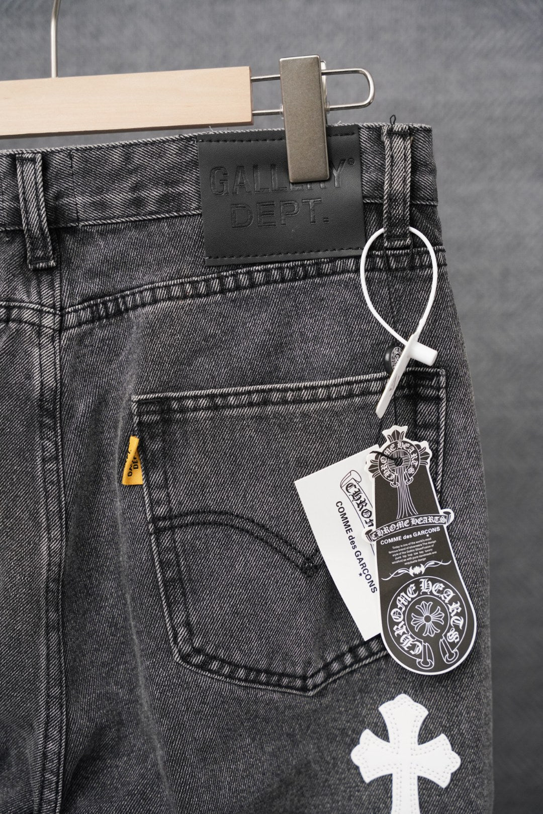 Dark denim pants with front pocket, belt loops, and white cross patch; hanging tag