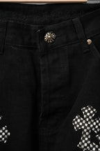 Black pants close-up of waistband button and stud; cross graphic patch detail.