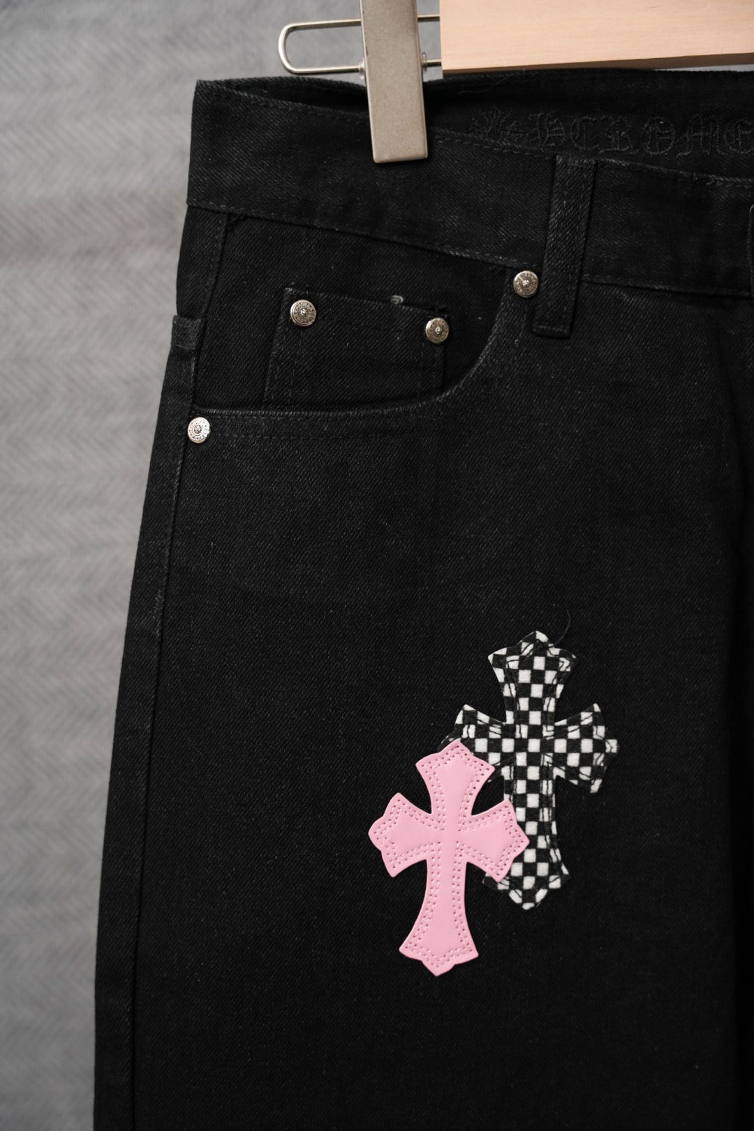 Black pants pocket close-up with pink cross and small checkered cross applique.
