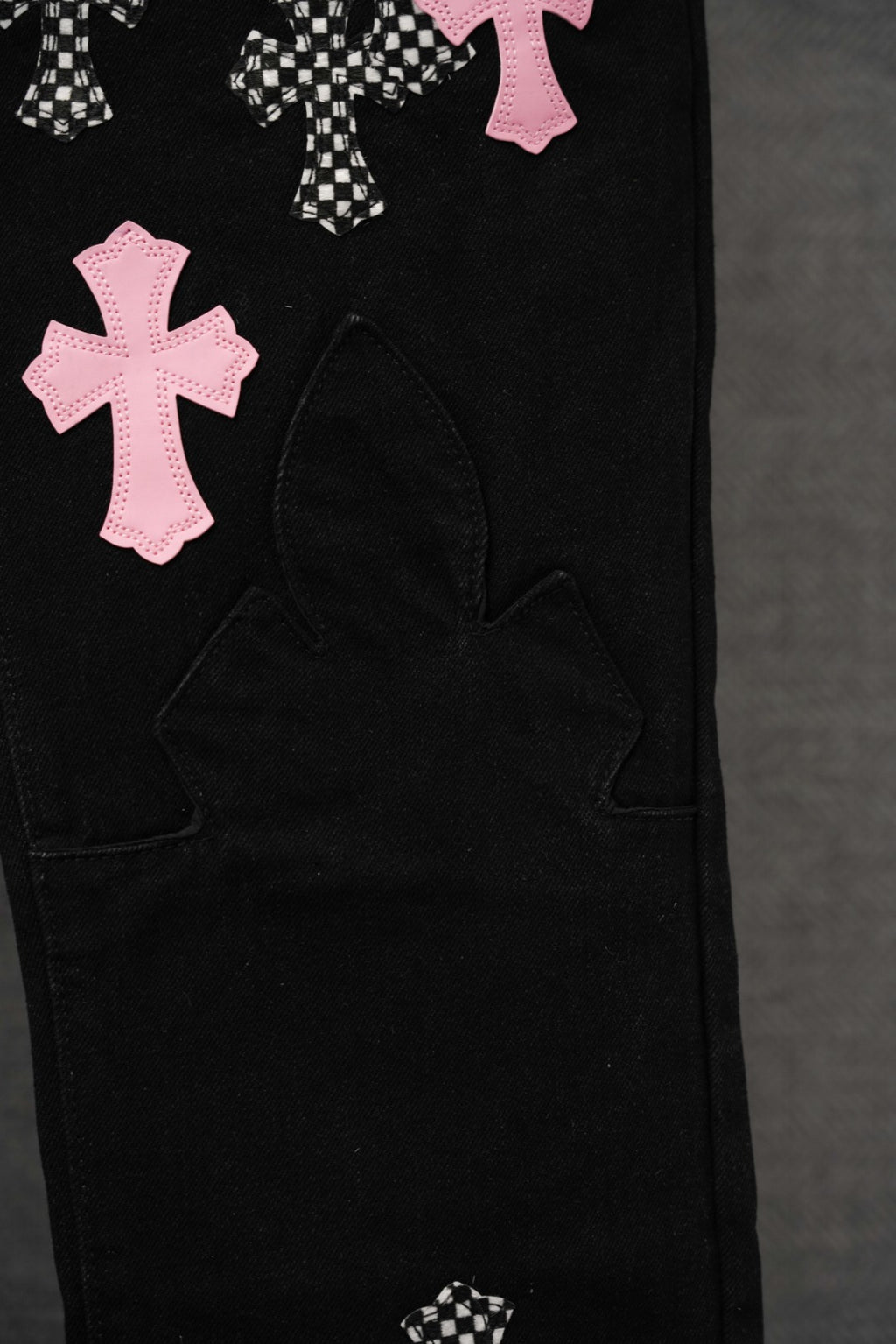 Black pants lower leg with pink cross applique and curved panel pocket stitching.