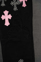 Black pants lower leg with pink cross applique and curved panel pocket stitching.