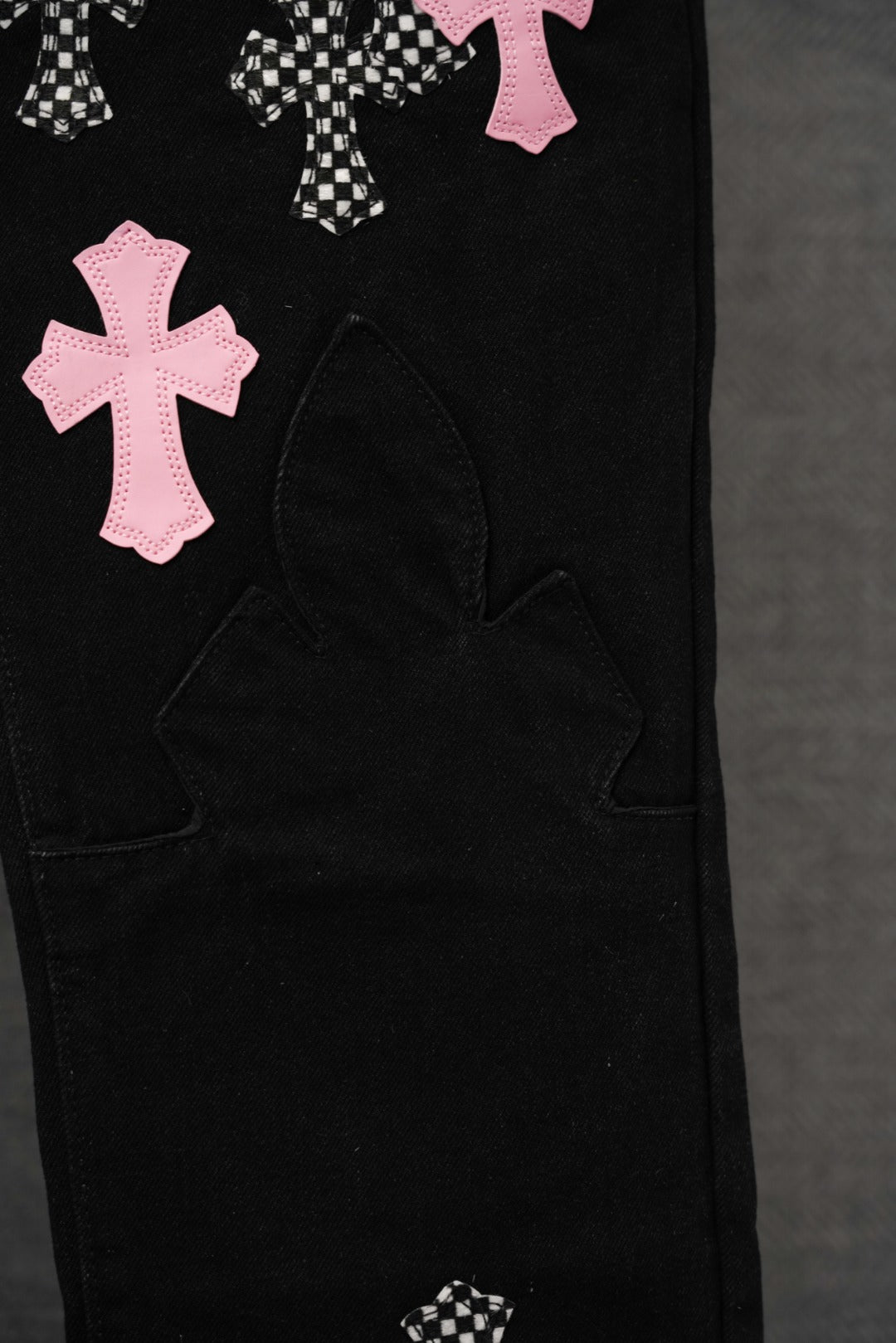 Black pants lower leg with pink cross applique and curved panel pocket stitching.