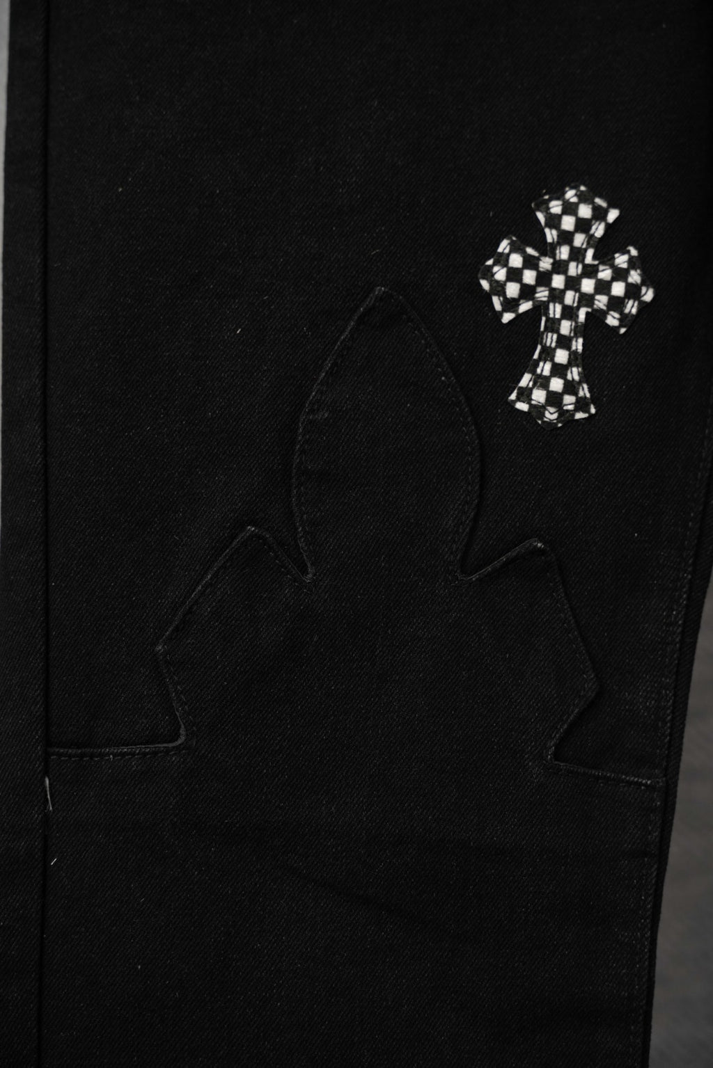 Black pants pocket area with small checkered cross patch and outlined cross motif.