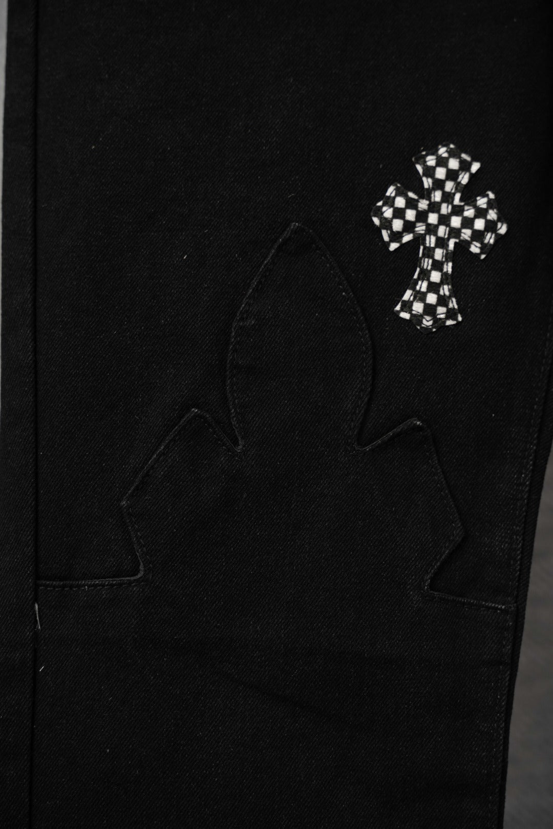 Black pants pocket area with small checkered cross patch and outlined cross motif.
