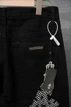 Black pants back view with back pocket, zipper, and checkered cross applique; hanging tag.