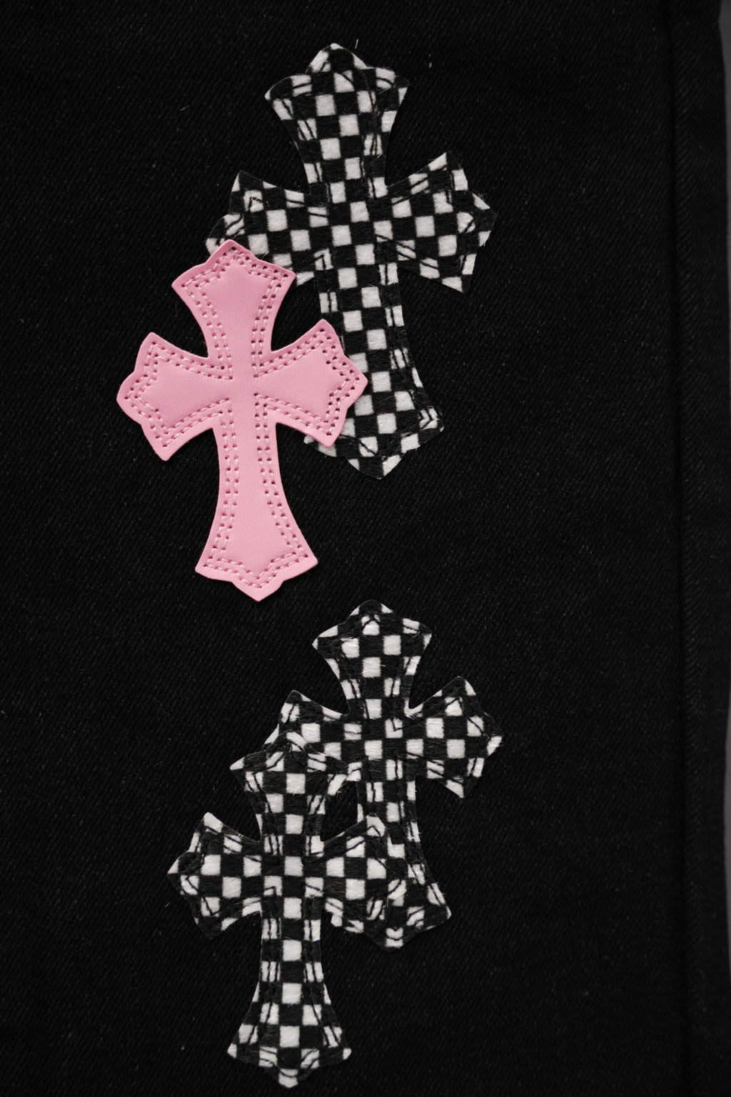 Black pants leg with large pink cross and two checkered cross patches.
