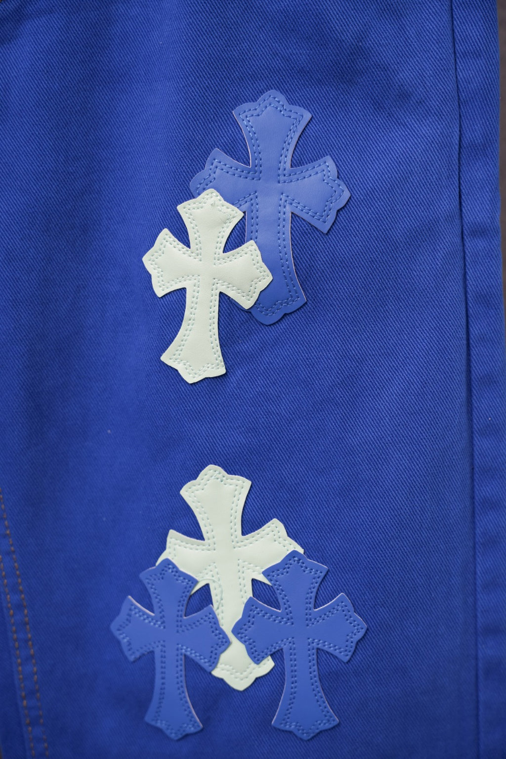 Blue pants leg close-up with large embroidered cross patches in light blue