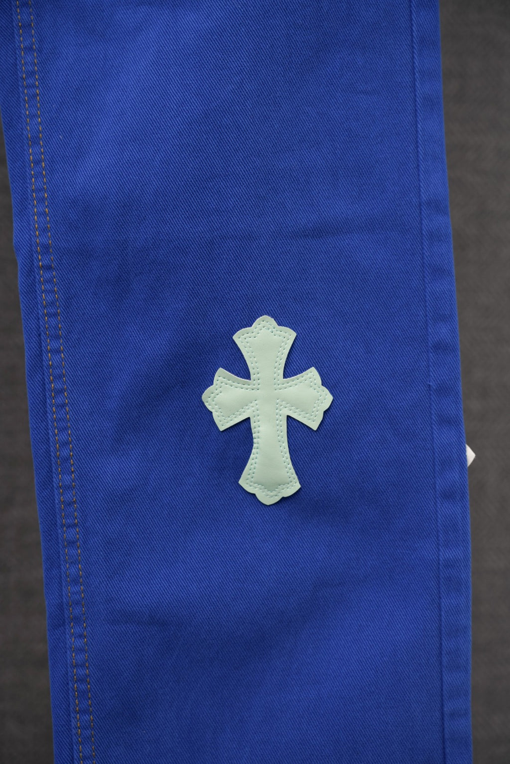 Blue pants leg close-up with single light blue embroidered cross patch