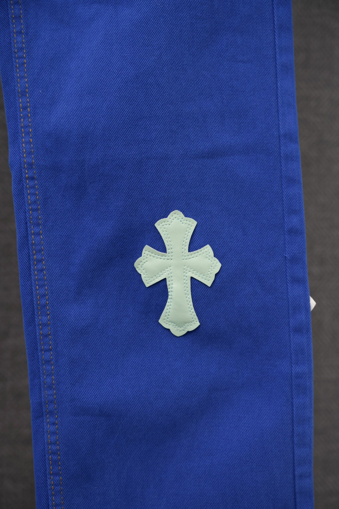 Blue pants leg close-up with single light blue embroidered cross patch