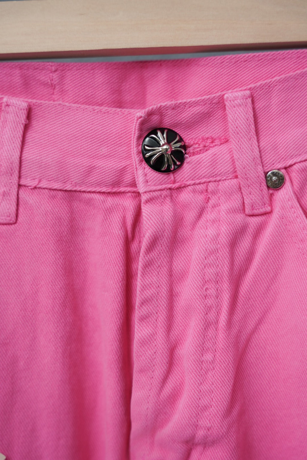 Pink denim pants waistband with black button and belt loops, close-up