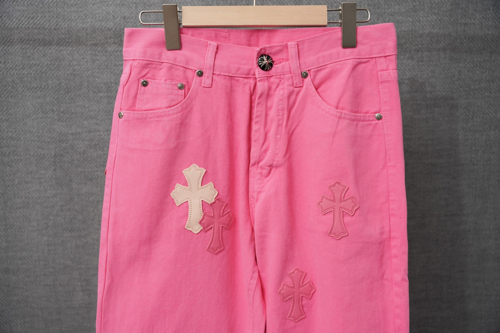 Pink denim pants with button fly, front pockets, and cross applique on legs