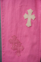 Pink denim pants with stitched cross applique details, close-up on leg