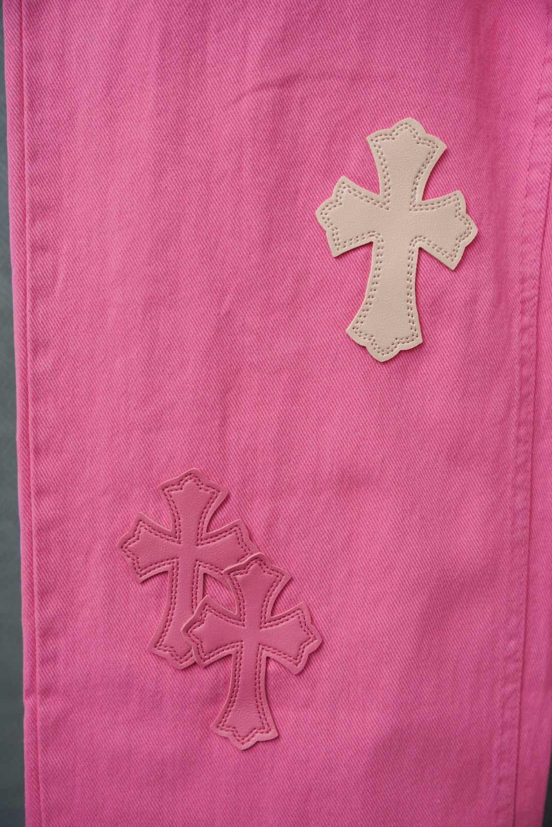 Pink denim pants with stitched cross applique details, close-up on leg