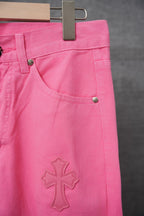Pink denim pants with front pocket, small cross applique, and black buttons