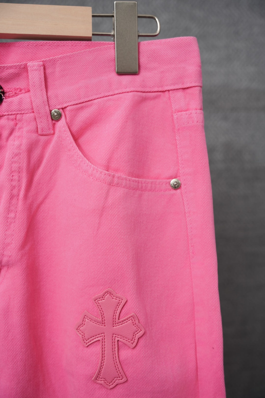 Pink denim pants with front pocket, small cross applique, and black buttons