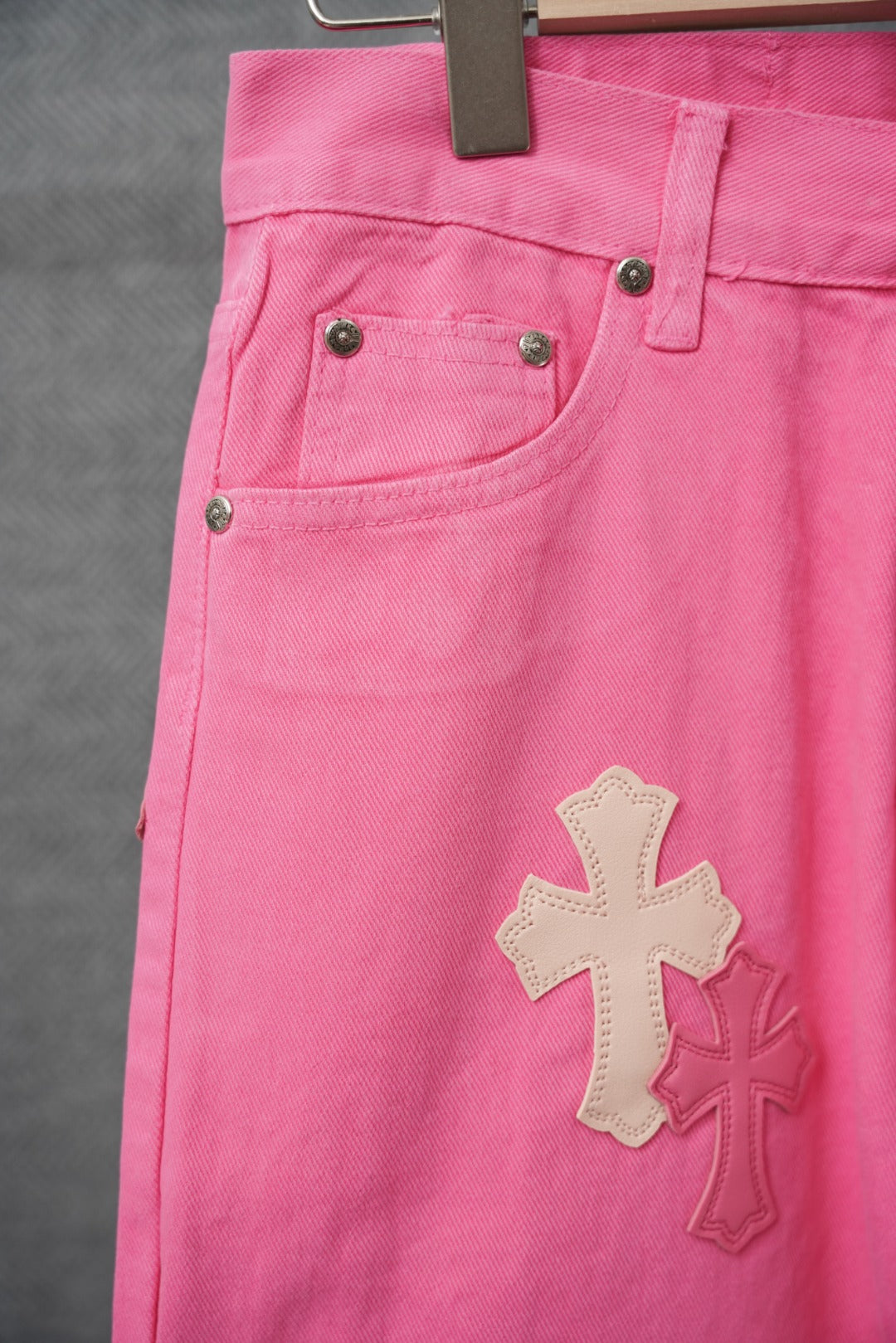 Pink denim pants with coin pocket and large cross applique near thigh