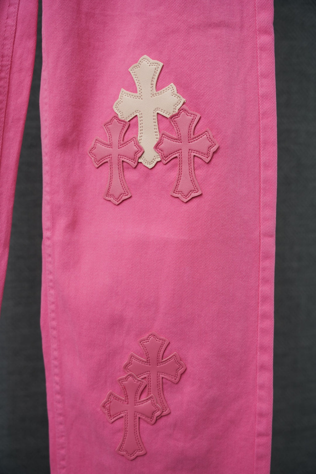 Pink denim pants with three cross appliqué graphics, close-up