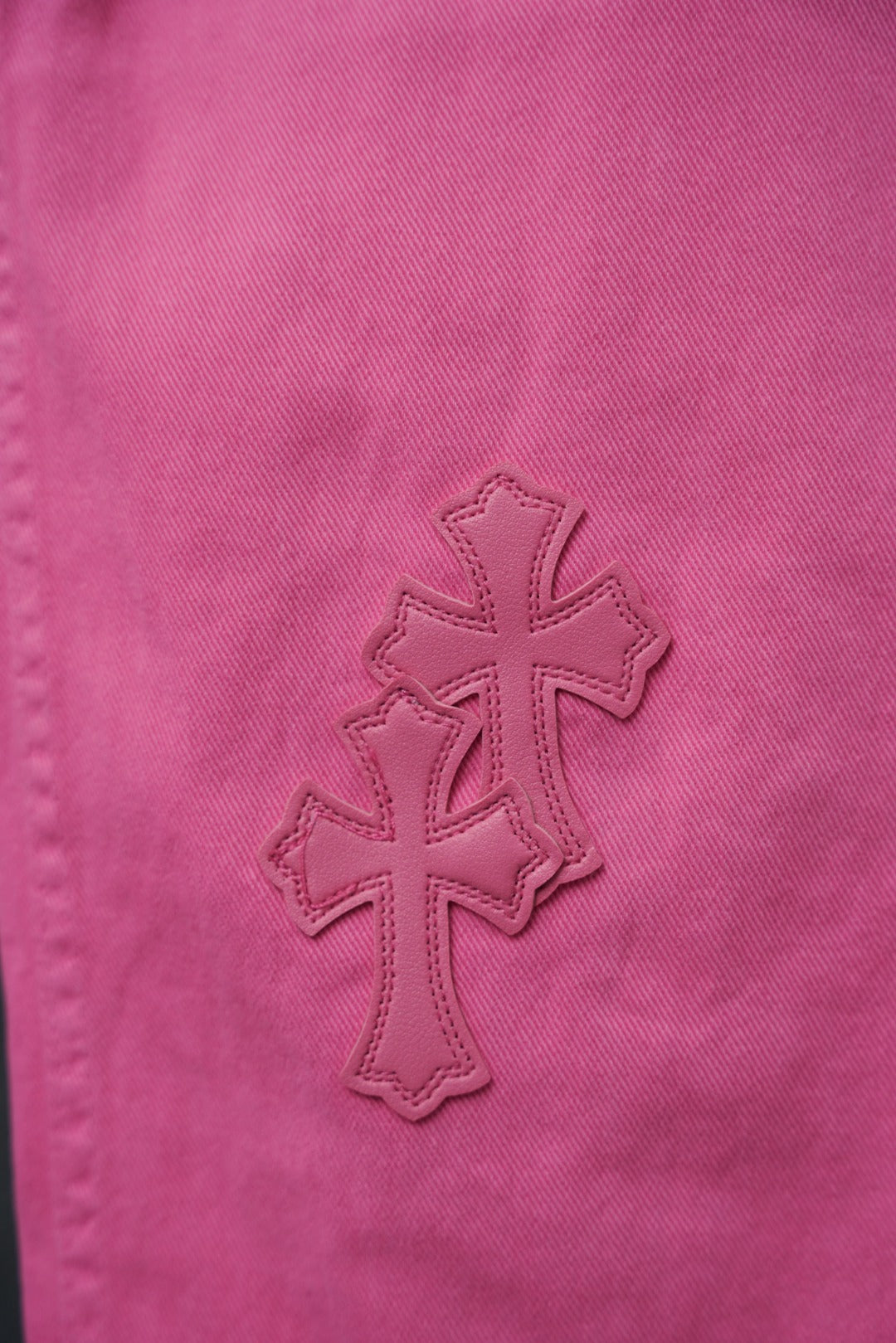 Pink chrome pants with cross-shaped embroidered appliques on the leg.