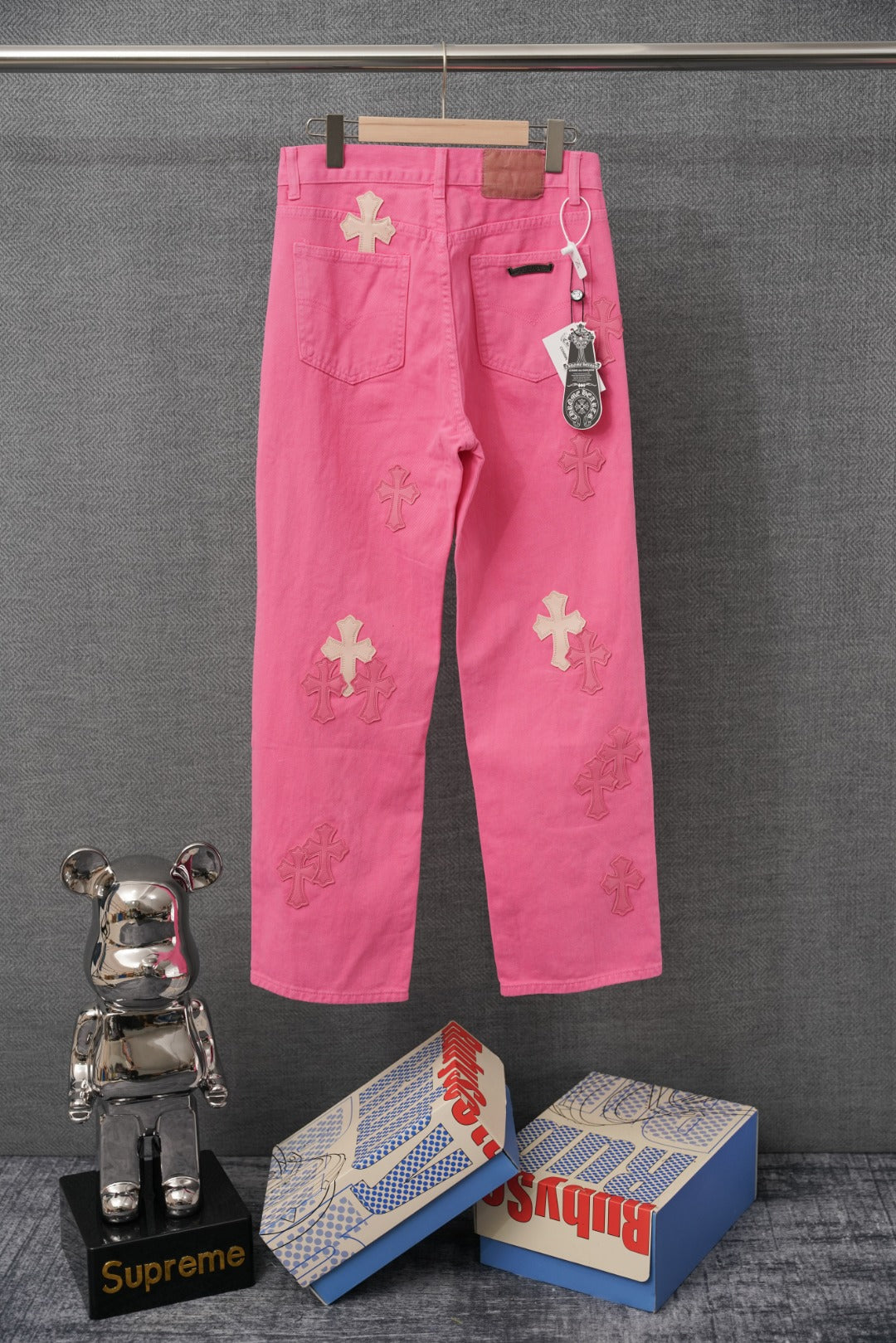 Pink denim pants with embroidered cross graphics, back view with belt loops