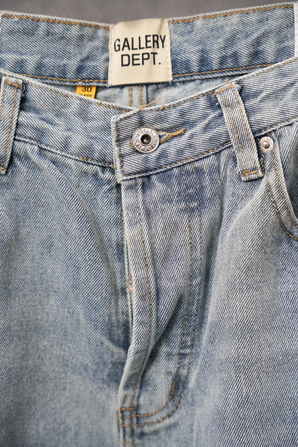 Light wash denim pants close-up of front button, belt loops, and stitching