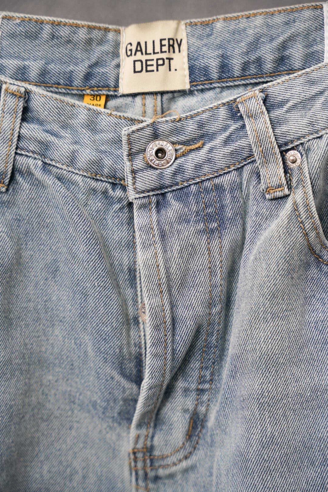 Light blue denim jeans waistband and button close with Gallery Dept. logo tag