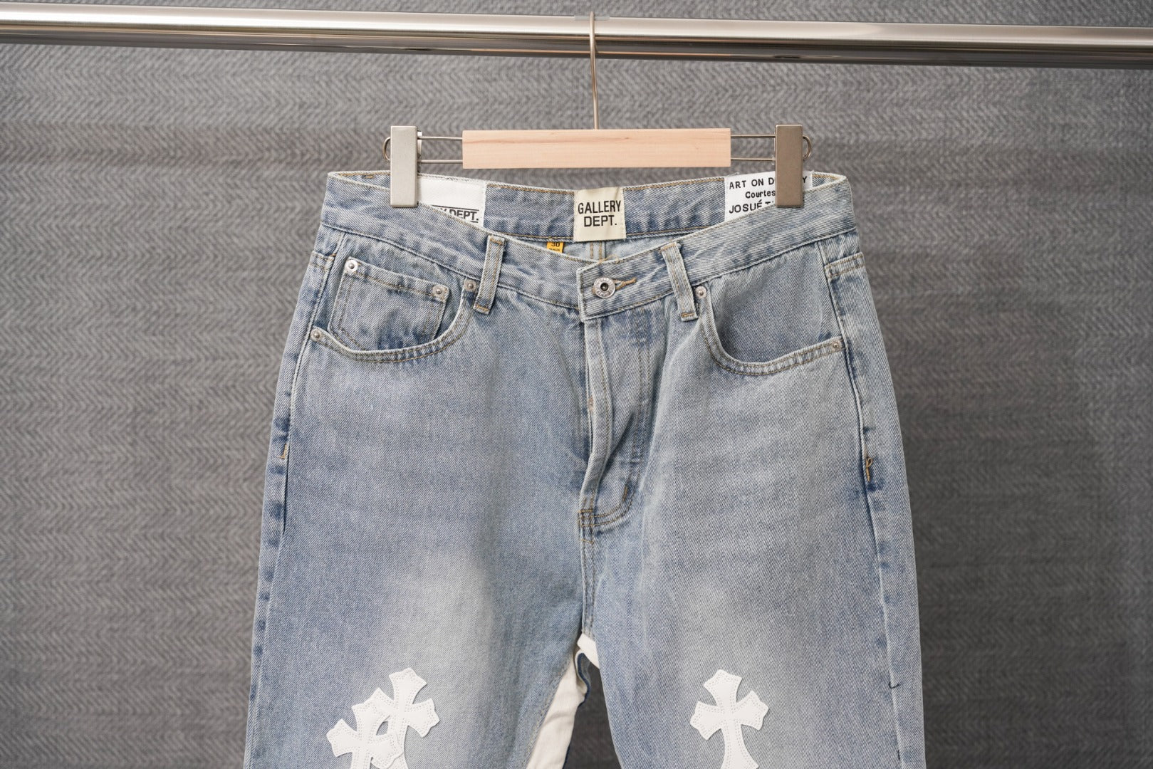 Light wash denim pants with button fly and white cross patches on legs