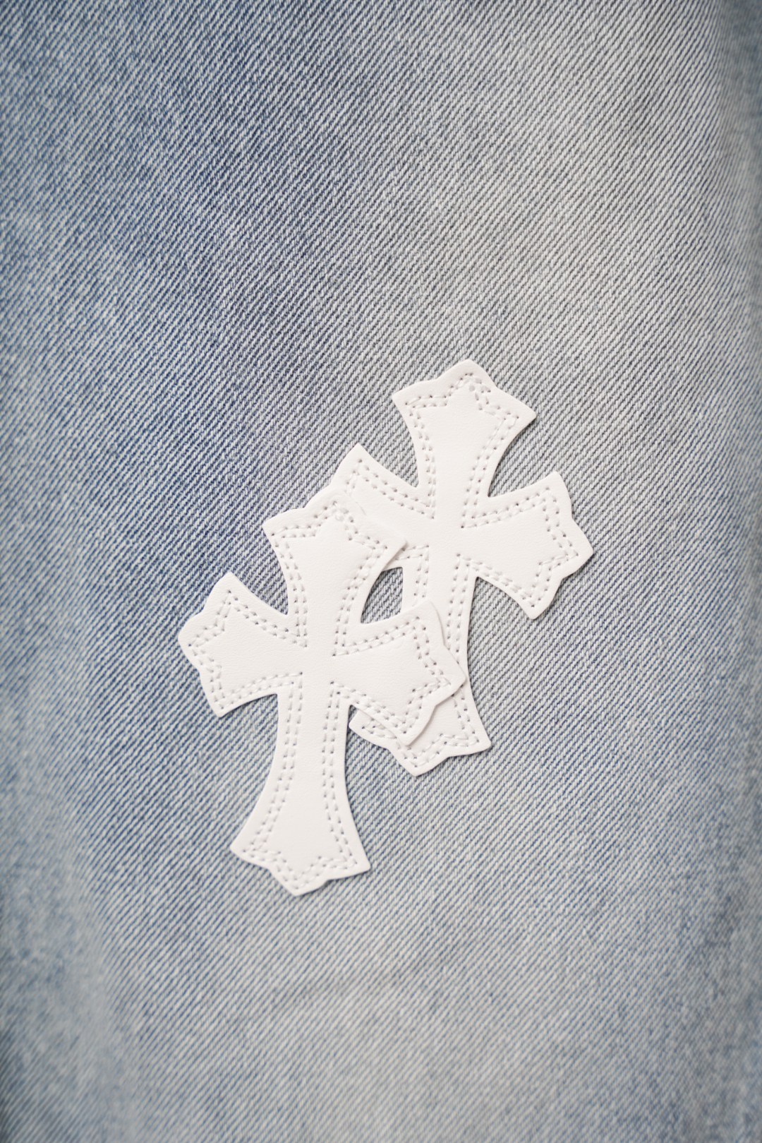 Light wash denim pants fabric with a white cross applique