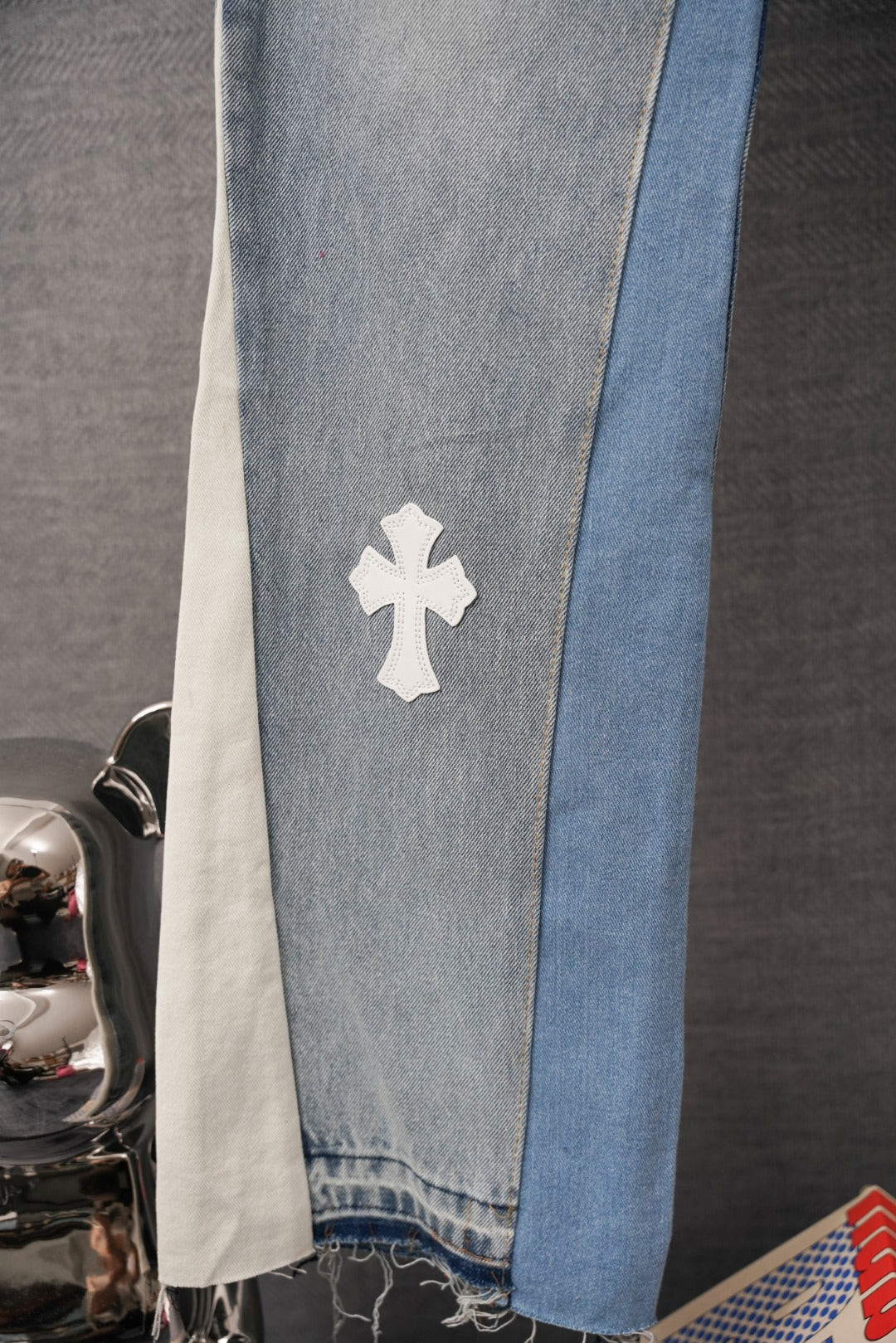 Light wash denim pants leg with white cross applique and blue side stripe