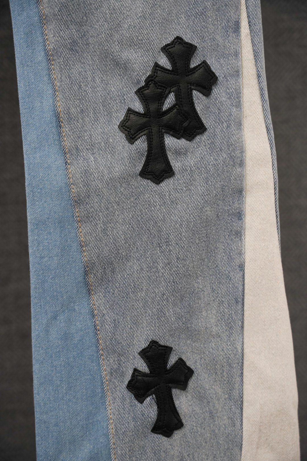 Light-wash denim pants leg with black cross patch and contrasting trim panel
