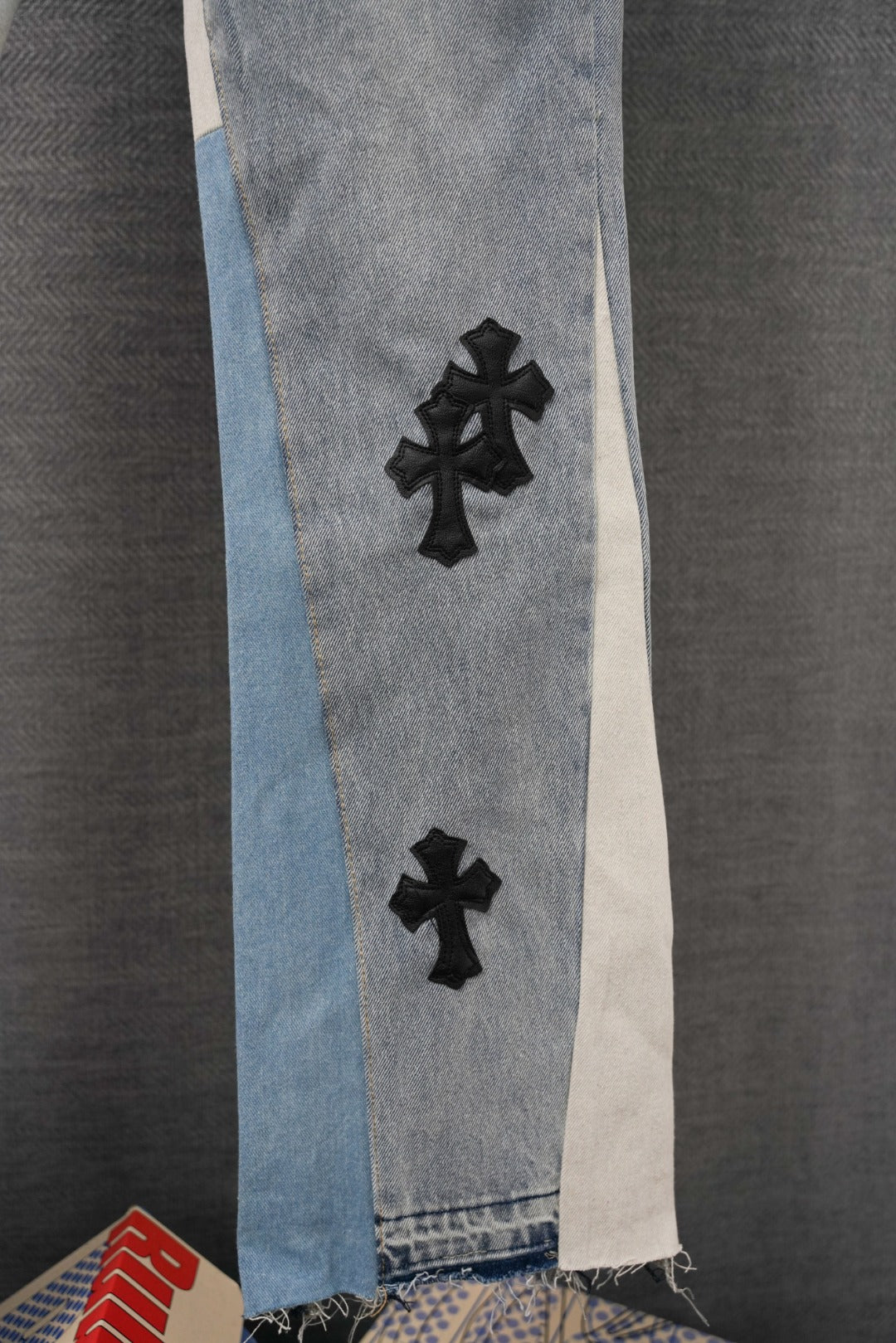 Light wash denim jeans with black cross applique and raw hem on side panel