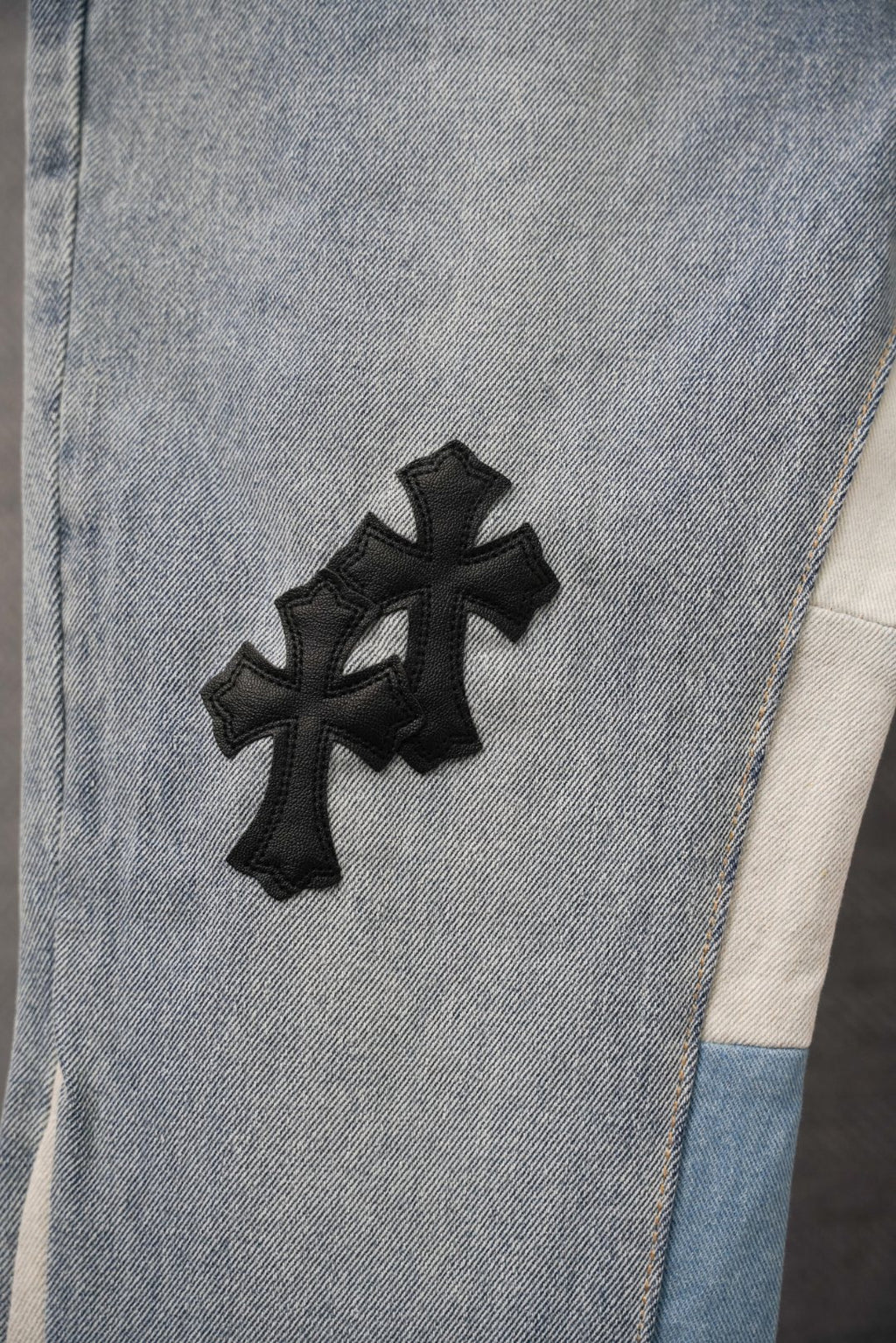 Light-wash denim pants leg with raised black cross patch detail
