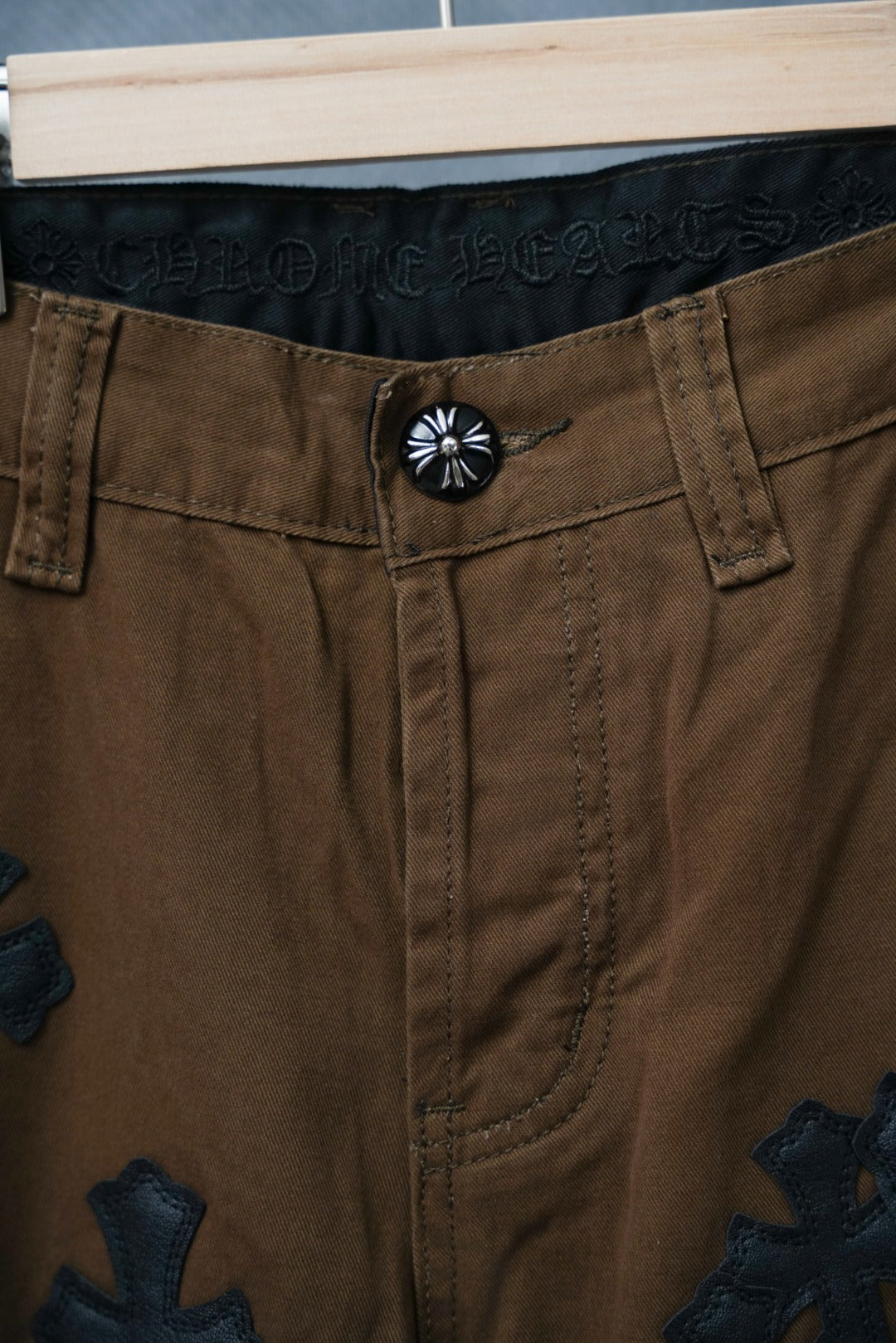 Brown pants with button waist and dark cross patch embroidery on leg