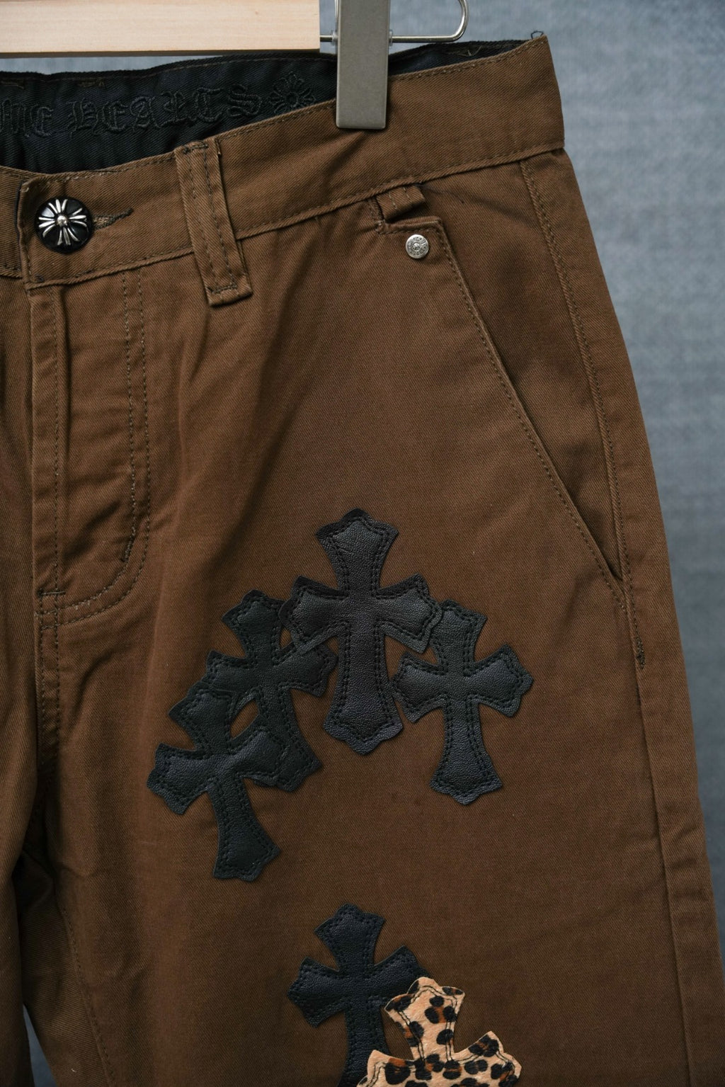 Brown pants with large dark cross embroidery and leopard-print cross near hem