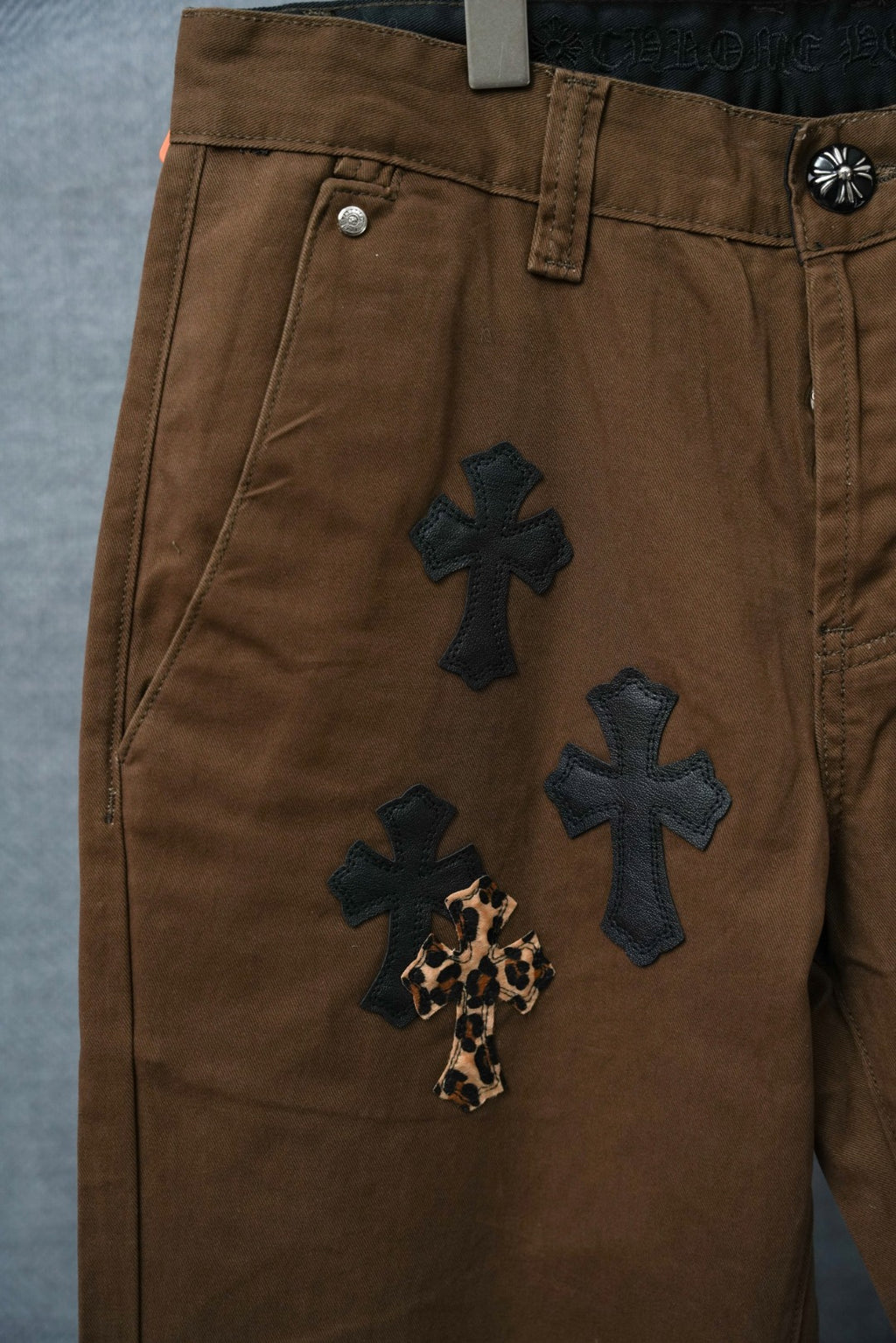 Brown pants with multiple dark cross patches and leopard-print cross accent